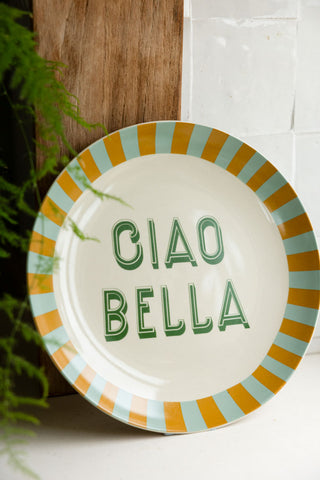 The Large White Ciao Bella Plate styled leaning against a wooden chopping board, styled next to a plant.