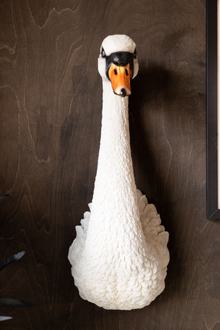 The Large White Faux Swan Head Wall Art displayed on a dark wall next to an art print and a plant.