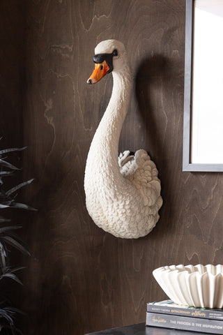 The Large White Faux Swan Head Wall Art displayed on a dark wall, styled with an art print, plant, ceramic bowl and some books.