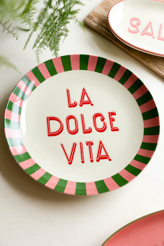 The Large White La Dolce Vita Plate styled with other colourful plates, a wooden chopping board and a plant.