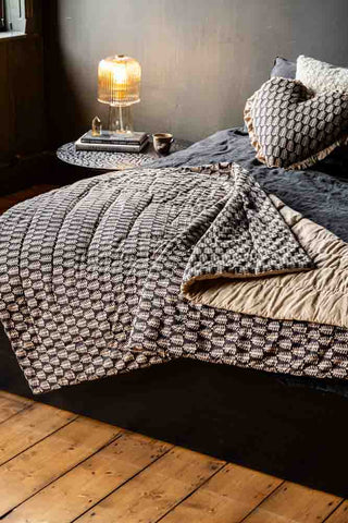 The Leaf Print Reversible Quilt in King-Size partially folded on a black bedset with an amber table lamp in the background.