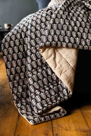 Close-up of the Leaf Print Reversible Quilt in King-Size draped over the corner of a black bed.