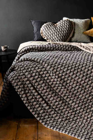 The Leaf Print Reversible Quilt in King-Size shown draped over a bed next to a black side table.