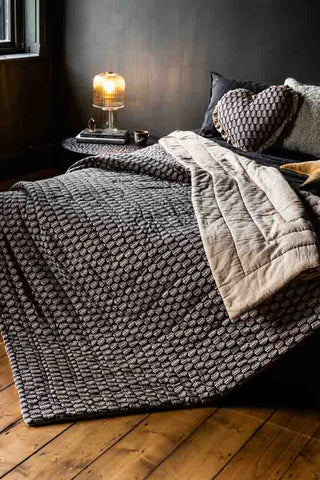 Lifestyle image of the Leaf Print Reversible Quilt in King-Size displayed on a bed in a room with black walls and wooden flooring.