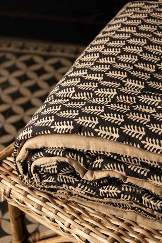 The Leaf Print Reversible Quilt in King-Size folded up and displayed on a wicker seat.