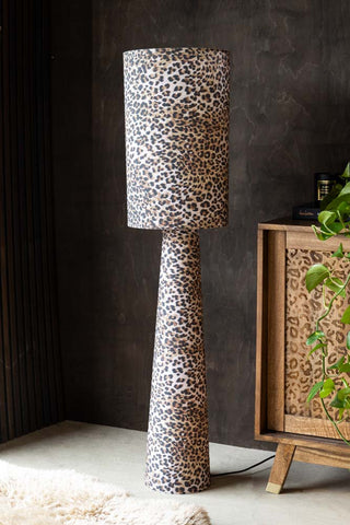 The Leopard Love Print Floor Lamp displayed next to a leopard print sideboard with a plant and rug, in front of a dark wall.