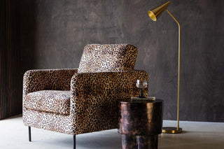 leopard print armchair styled with a mottled copper side table, brass floor lamp and black wine glass.