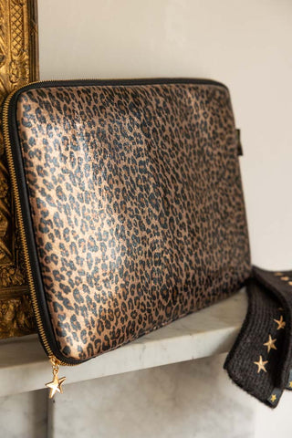 The Leopard Print 15-Inch Laptop Case with a laptop inside, displayed on a shelf with some handwarmers and a decorative gold frame.