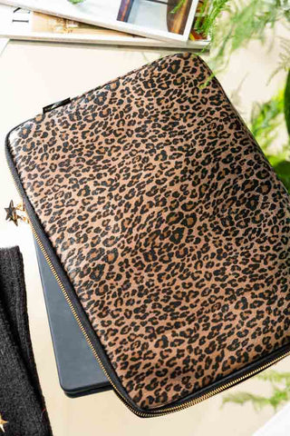 The Leopard Print 15-Inch Laptop Case displayed on a surface with some magazines and a plant.