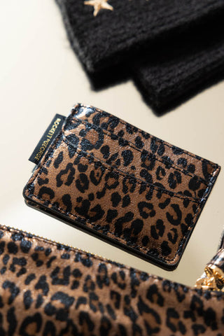 The Leopard Print Card Holder displayed on a surface with a leopard print bag and some handwarmers.