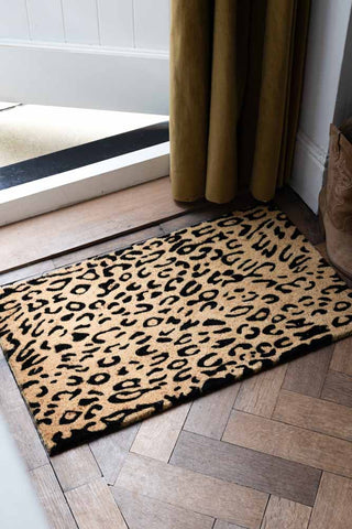 The Leopard Print Coir Doormat styled by an open door, with some shoes and a door curtain.