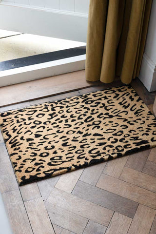 The Leopard Print Coir Doormat displayed by an open door.