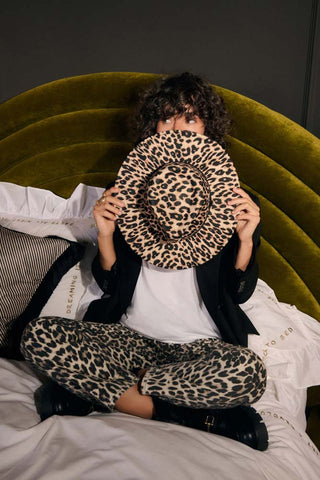 The Leopard Print Fedora being held by a model sitting cross-legged on a bed.