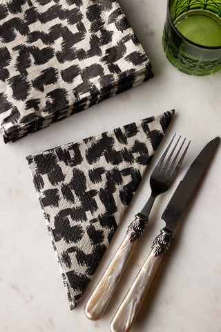 The Abstract Leopard Print Napkins styled on a table with a knife, fork and green glass.