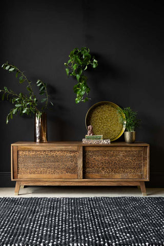 The Leopard TV Unit styled in front of a dark wall with various home accessories, plants and a rug.