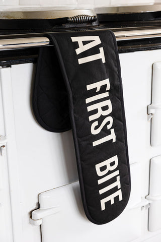 The Love At First Bite Black Oven Gloves styled hanging from a rail on the front of an oven.