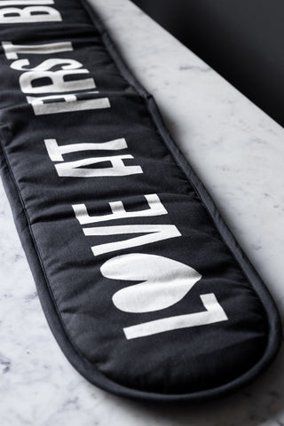 The Love At First Bite Black Oven Gloves laid flat across a white marble surface.