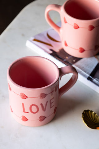 Two of the Love Hand-Painted Cappuccino Mug displayed on a surface with a spoon and a magazine, seen from above.