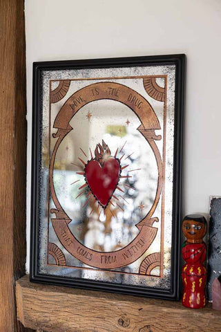 The Love Is The Drug Decorative Mirror styled in front of a white wall on a wooden beam with some ornaments.