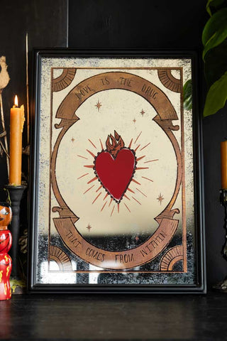 The Love Is The Drug Decorative Mirror styled on a black surface with candlestick holders and greenery.