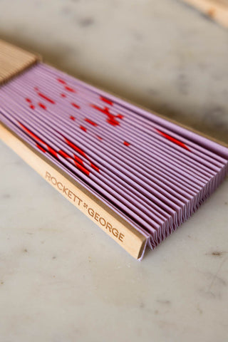 Close-up of the Love Is The Drug Pink & Red Fan folded up on a white marble table.