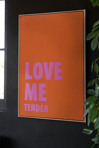 The Love Me Tender Canvas displayed on a black wall next to a window and a plant.