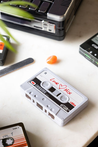 The Love Mix Cassette Tape Storage Tin styled on a marble surface with other accessories and a plant.