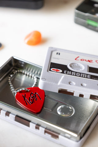 Detail shot of the Love Mix Cassette Tape Storage Tin with a keyring shaped like a guitar pick inside. 