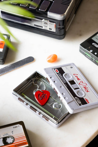 The Love Mix Cassette Tape Storage Tin styled with the lid off on a white surface with other tins, various accessories and a plant.