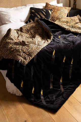 The Reversible Black Lovestruck & Leopard Print Throw draped across a bed, showing both sides of the design.