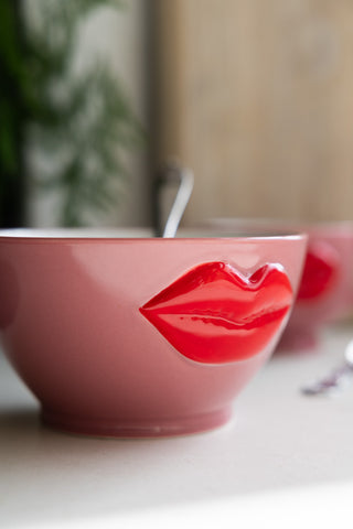 Stylish pink cereal bowl featuring bold red lips in a 3D design, with a spoon resting inside, set on a white table.