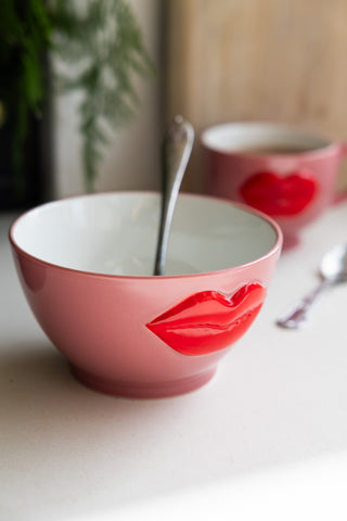 Fun pink cereal bowl adorned with a glossy 3D red lips motif, holding a spoon, ready for a meal.