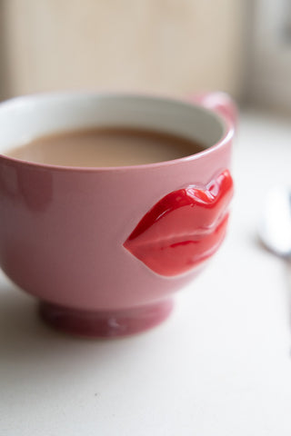 Whimsical pink mug adorned with shiny red lips in 3D, filled with a warm cup of tea.