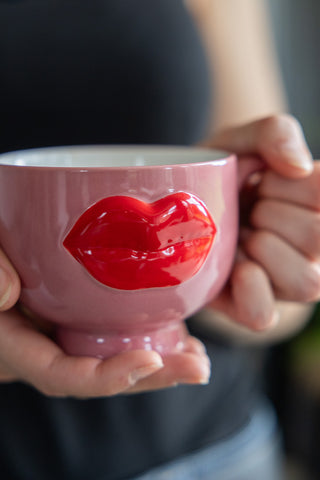 Playful pink mug featuring bold red lips in a 3D design held in someones hands.