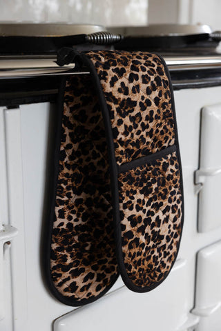 A set of leopard print oven gloves displayed hanging from the front of an oven.