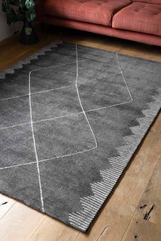 Close-up of the Mason Black Diamond Rug styled on a wooden floor in a living room.