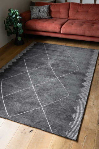 The Mason Black Diamond Rug styled on a living room floor in front of a sofa and plant.