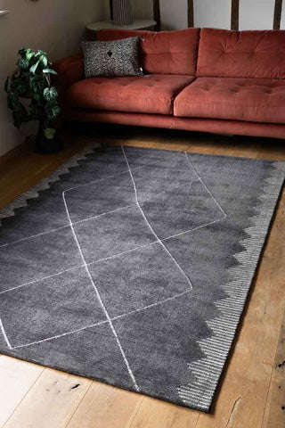 The Mason Black Diamond Rug styled on a wooden floor in a living room.