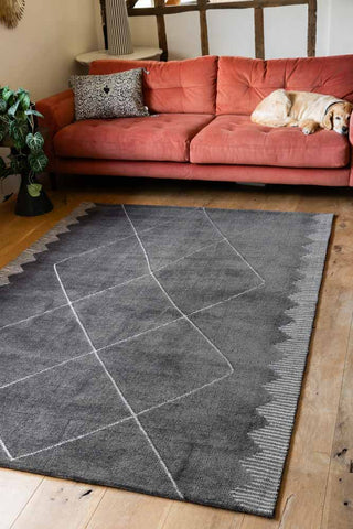 The Mason Black Diamond Rug styled in a living room with a dog on a sofa in the background.