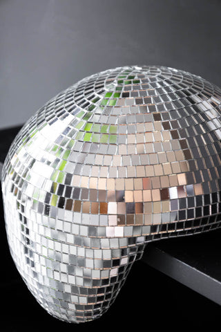 Extreme close-up of a silver disco mirror ball, designed to look as though it's melting off the edge of a sideboard 