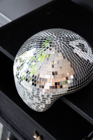 Overhead view of silver disco mirror ball, designed to look as though it's melting off the edge of a black sideboard 