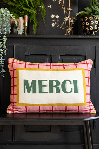 The Merci Cushion on a bench, displayed in front of the doors of a black sideboard.