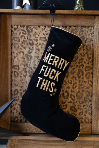 The Merry Fuck This Black Christmas Stocking hanging in front of a leopard print unit, styled with Christmas decorations.