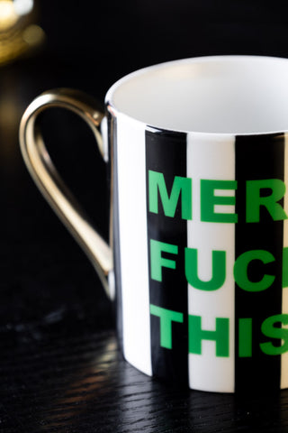 Close-up of the Merry Fuck This Stripe Mug displayed on a dark wood surface.