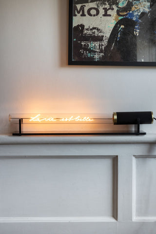 The Message In A Tube Light - La Vie Est Belle displayed on the frame in front of the wall, beneath an art print.