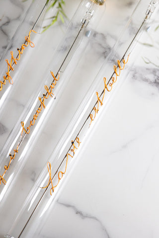 Close-up of the Message In A Tube Light - La Vie Est Belle with other versions on a white marble table.