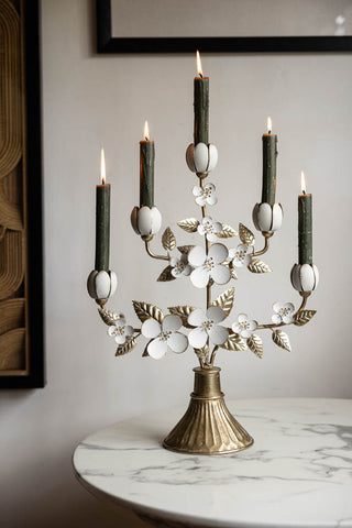 The Metal Floral Candelabra displayed with lit candles inside on a white round table.