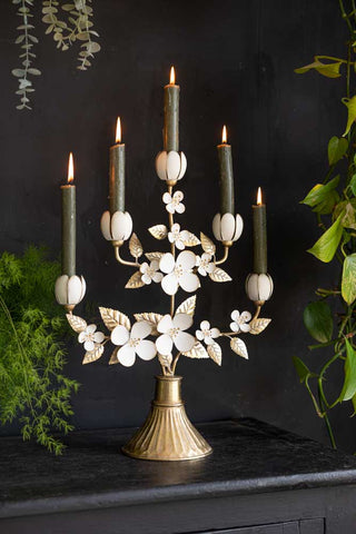 The Metal Floral Candelabra styled with lit candles inside, surrounded by greenery.