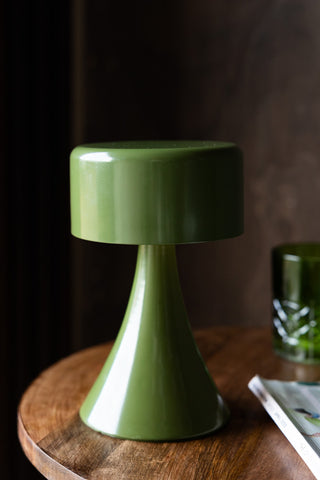 The Metal Mood Lighting Cordless Table Lamp in Green styled on a wooden table with a magazine and a green glass.