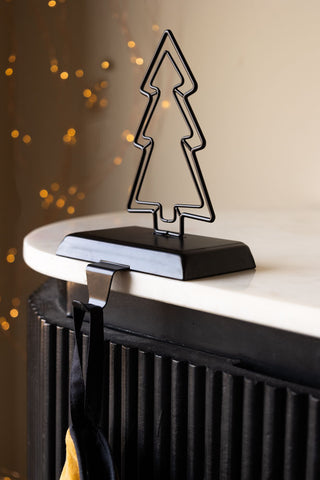 The Metal Tree Stocking Holder on the edge of a table with a stocking hanging from it.